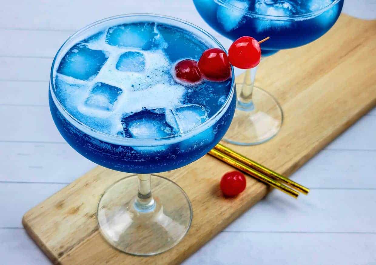 Two blue ocean water cocktails garnished with cherries.