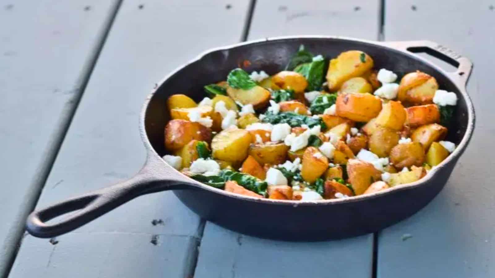 This photo shows a cast iron skillet with oven roasted potatoes with spinach and garlic on a blue wooden background.