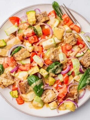 An overhead image of panzanella salad served on a white plate with dressing on top of it.