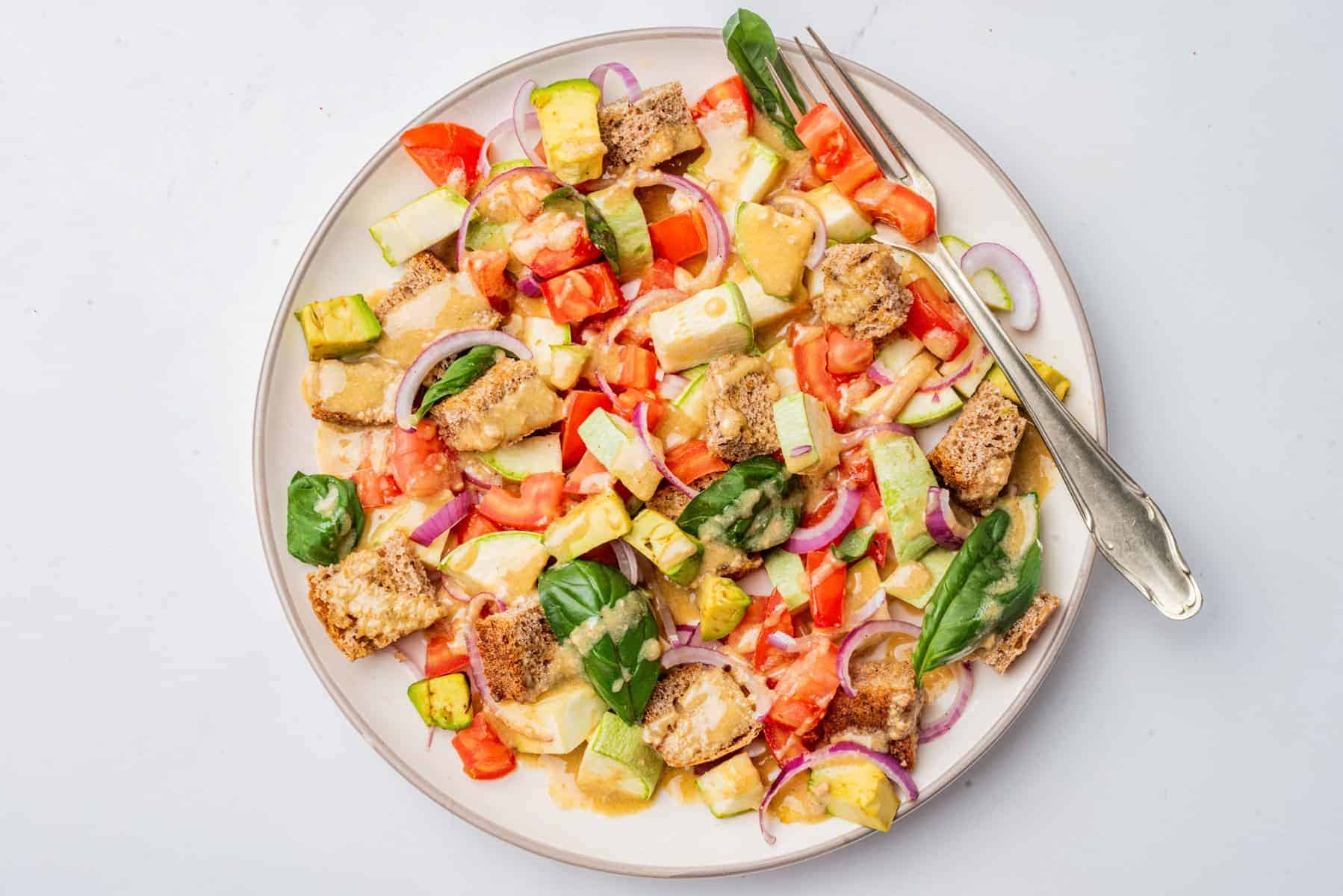 An overhead image of panzanella salad served on a white plate with dressing on top of it.