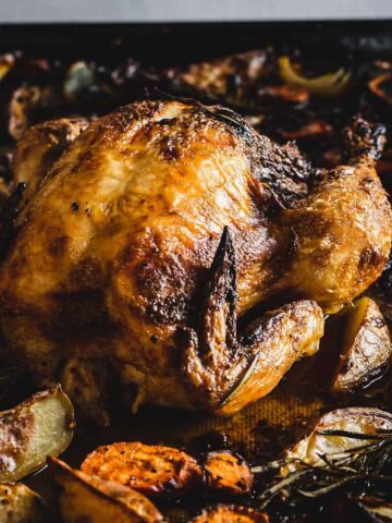 Hands holding paprika chicken and vegetables on a sheet pan.