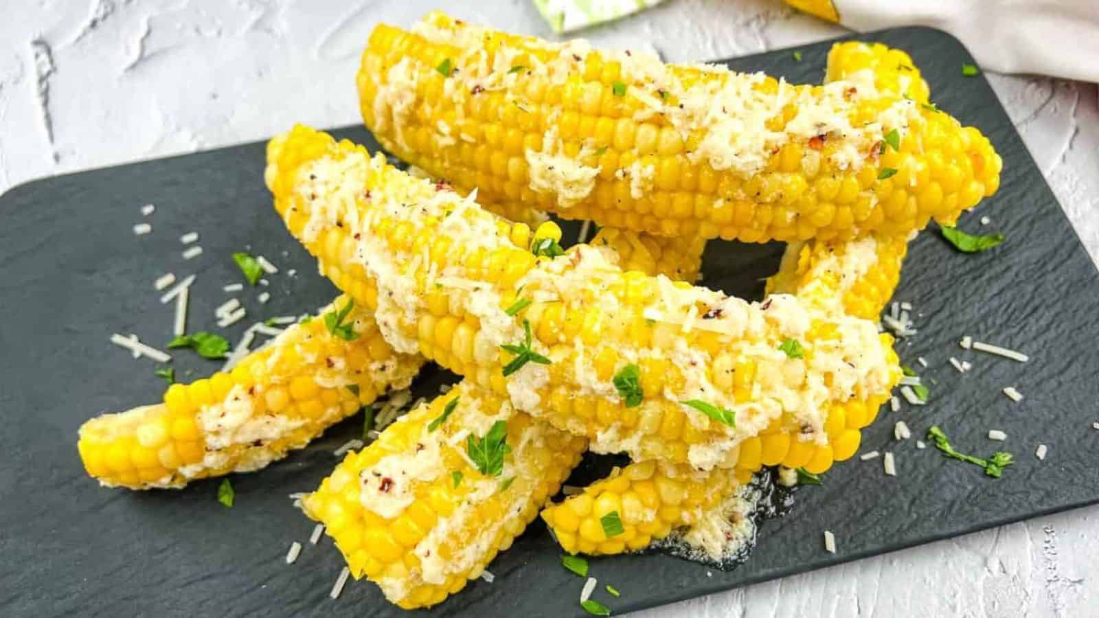 Corn on the cob with garlic parmesan on a black plate.