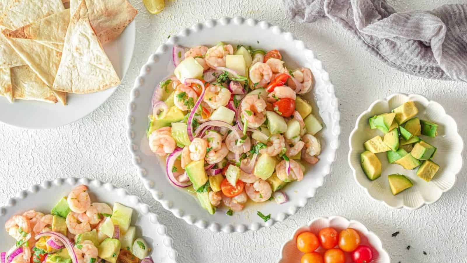 A plate of shrimp ceviche with tomatoes, cucumbers, and tortilla chips.