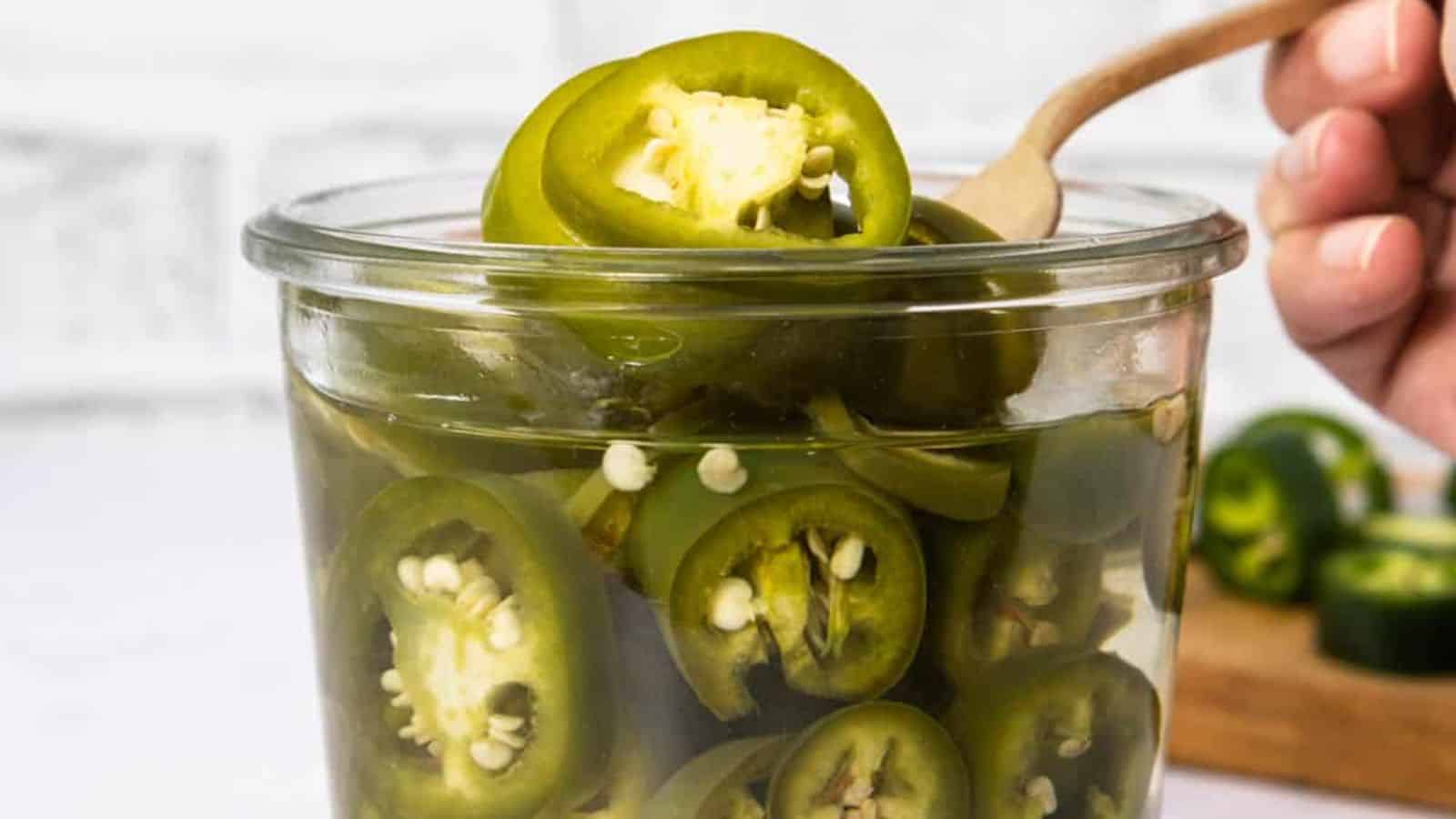 A close-up image of pickled jalapenos in a glass jar being scooped with a fork.