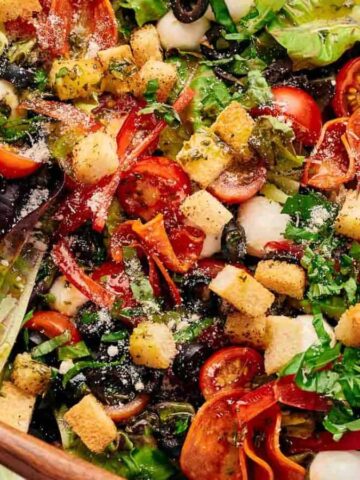 Homemade pizza salad in a serving bowl with wooden salad servers resting on top.