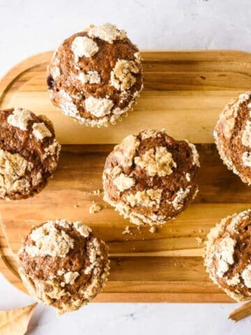 Overhead view of five pumpkin muffins on a wooden platter.