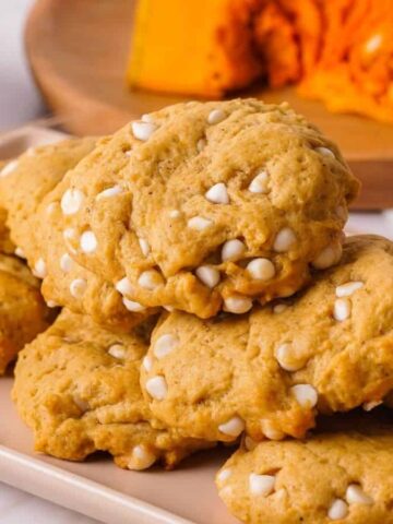 A plate of pumpkin cookies with white chocolate chips is displayed on a table.