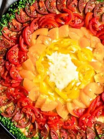 Rainbow Pizza filled with colorful tomatoes and green fresh chives around it.