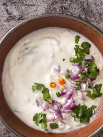 An overhead view of homemade raita served in a brown bowl.