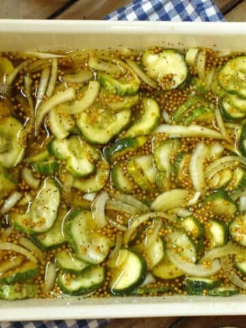 Bread and butter pickles in brine in a white dish.
