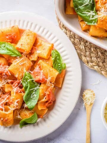 Overhead view of rigatoni arrabbiata dish placed on a white plate and baking dish. 