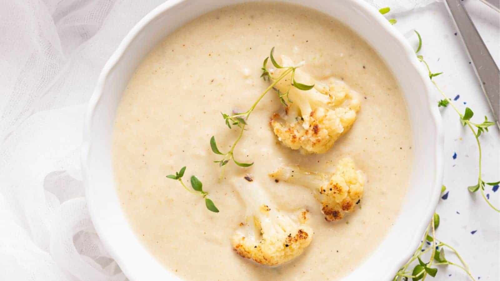 An image of roasted cauliflower soup in a white bowl, with fresh thyme on the side.