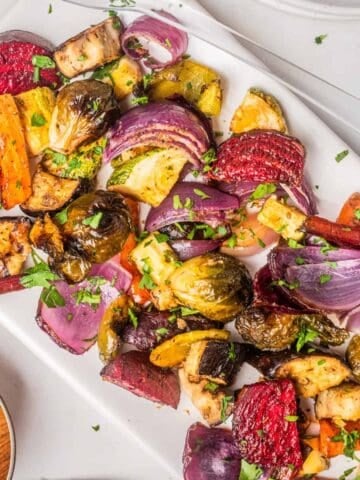 An overhead image of roasted vegetable salad on a serving dish. with the dressing on the side.