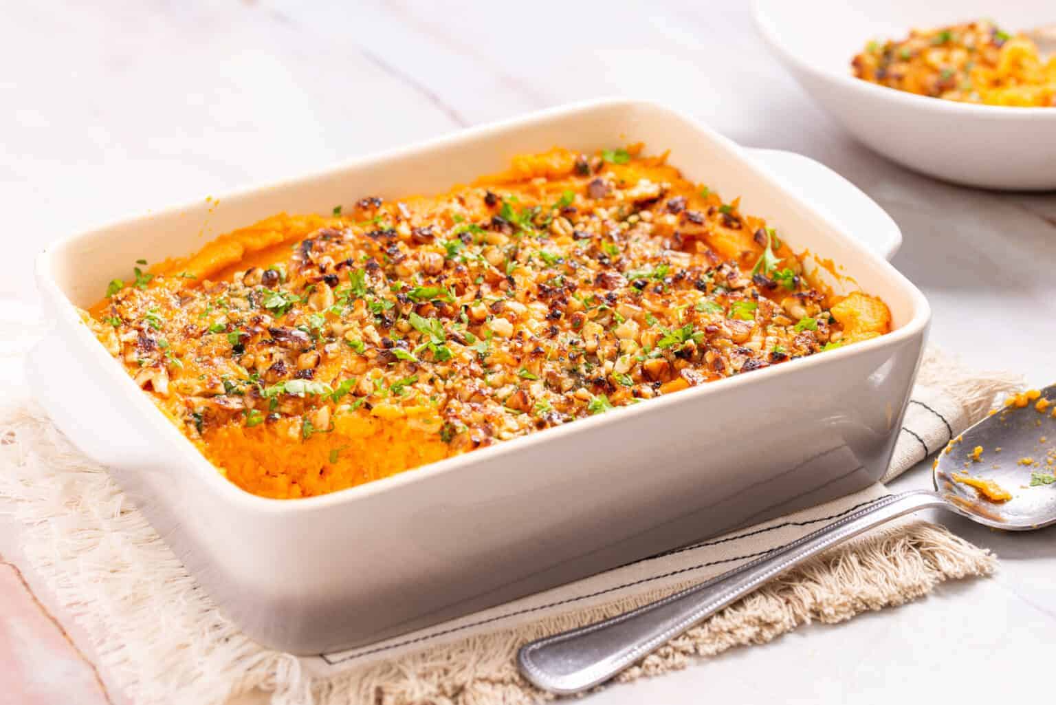 An angled shot of savory sweet potato casserole served in a baking dish.