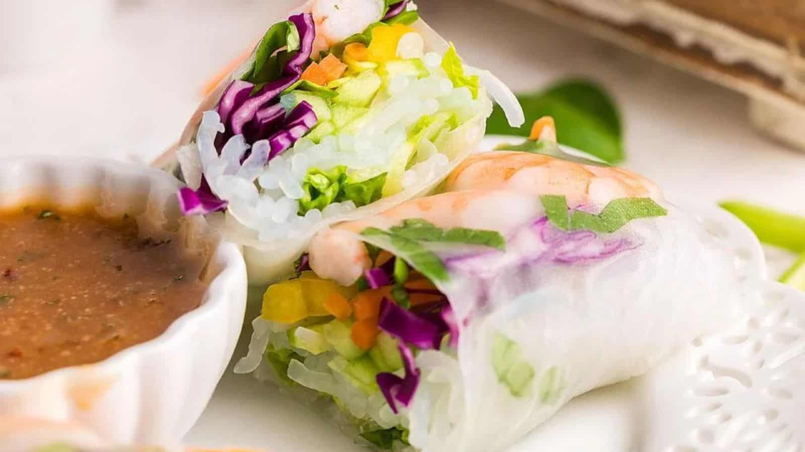 Close-up of halved shrimp spring rolls stacked on top of each other with spicy garlic sauce.