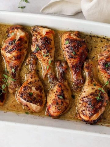 A white baking dish with chicken drumsticks layered inside and honey mustard sauce on top.