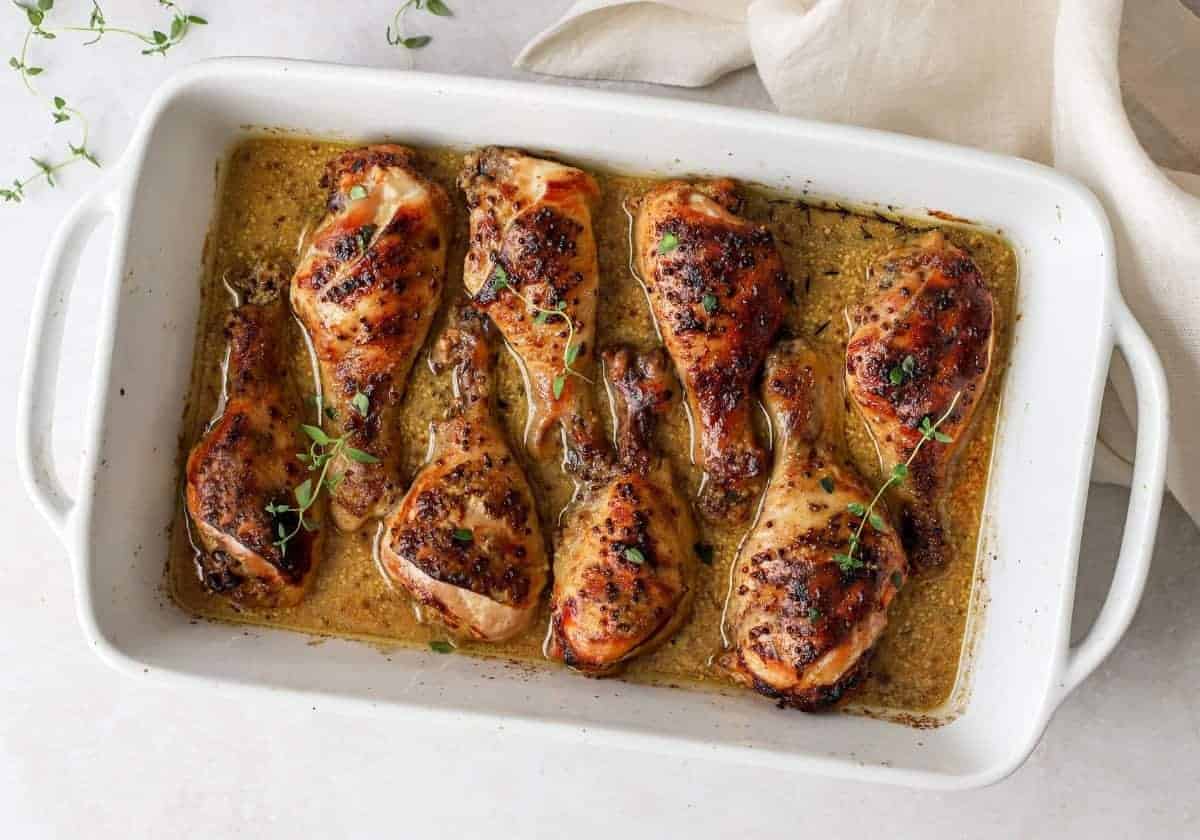 A white baking dish with chicken drumsticks layered inside and honey mustard sauce on top.
