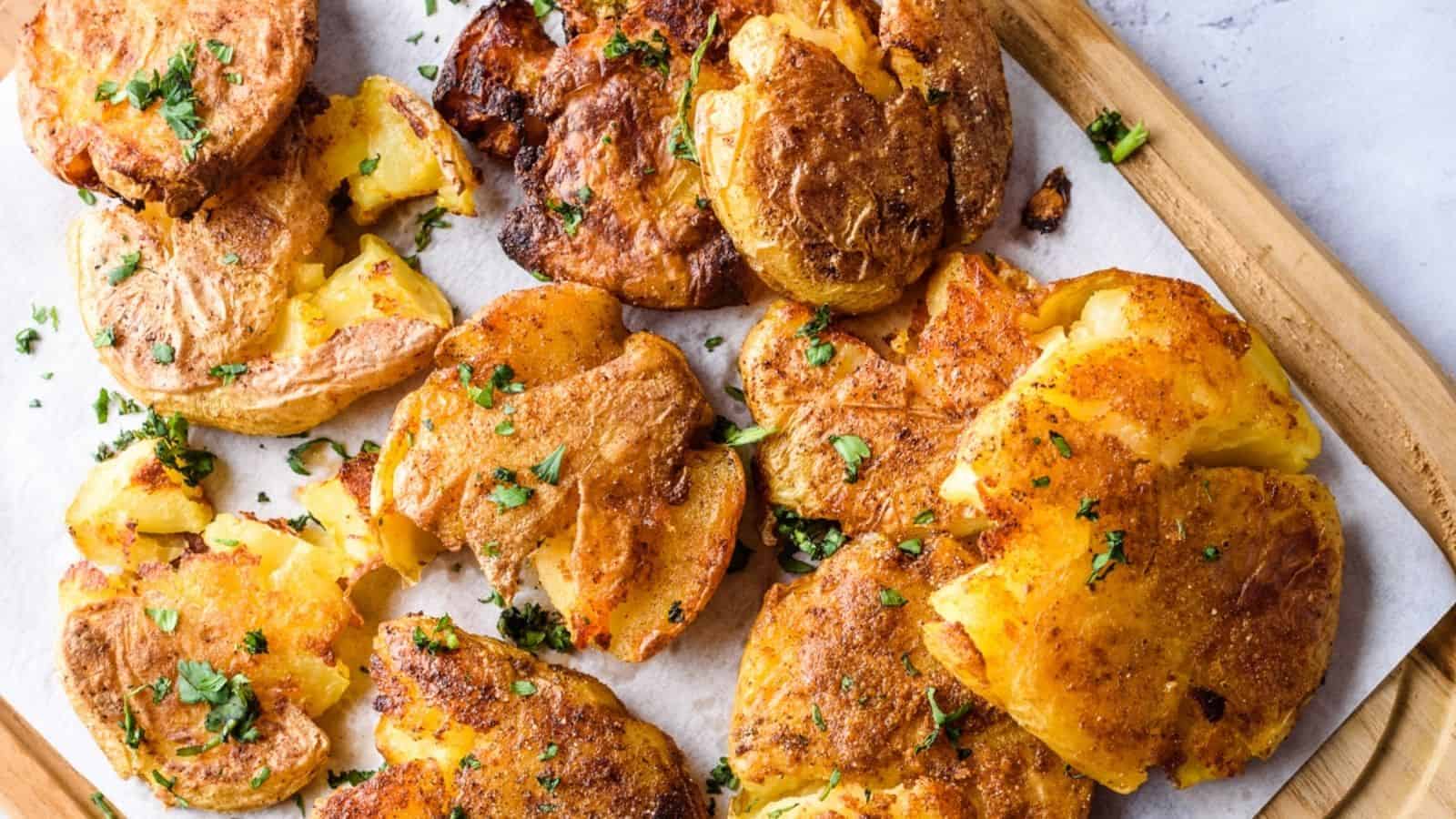 Smashed potatoes on a wooden board, crispy and golden, topped with fresh herbs.