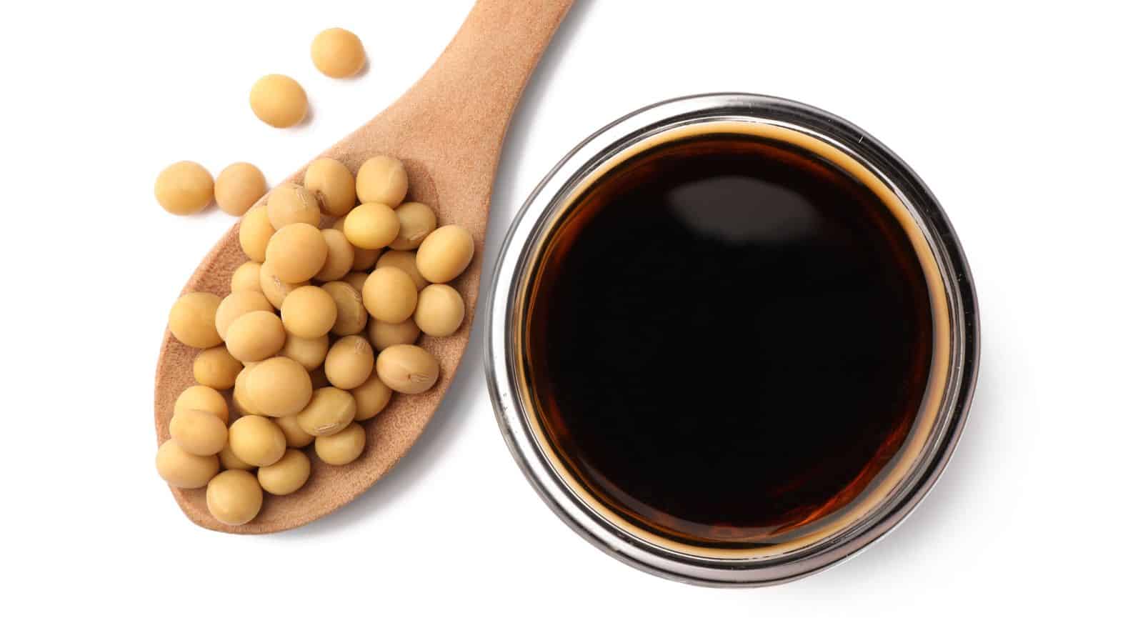 Bowl of soy sauce and spoon with soybeans isolated on white, top view.