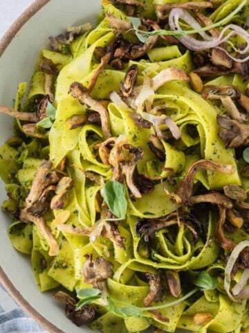 Top view of bowl of spring pasta with peas and oyster mushrooms with garnishes on the side.