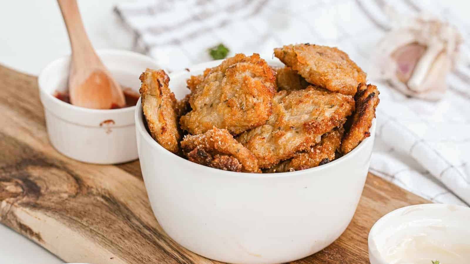 Cauliflower nuggets in a white bowl with dip in the background.