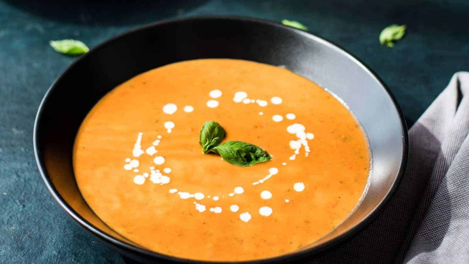 A black bowl of tomato basil bisque on a blue background.