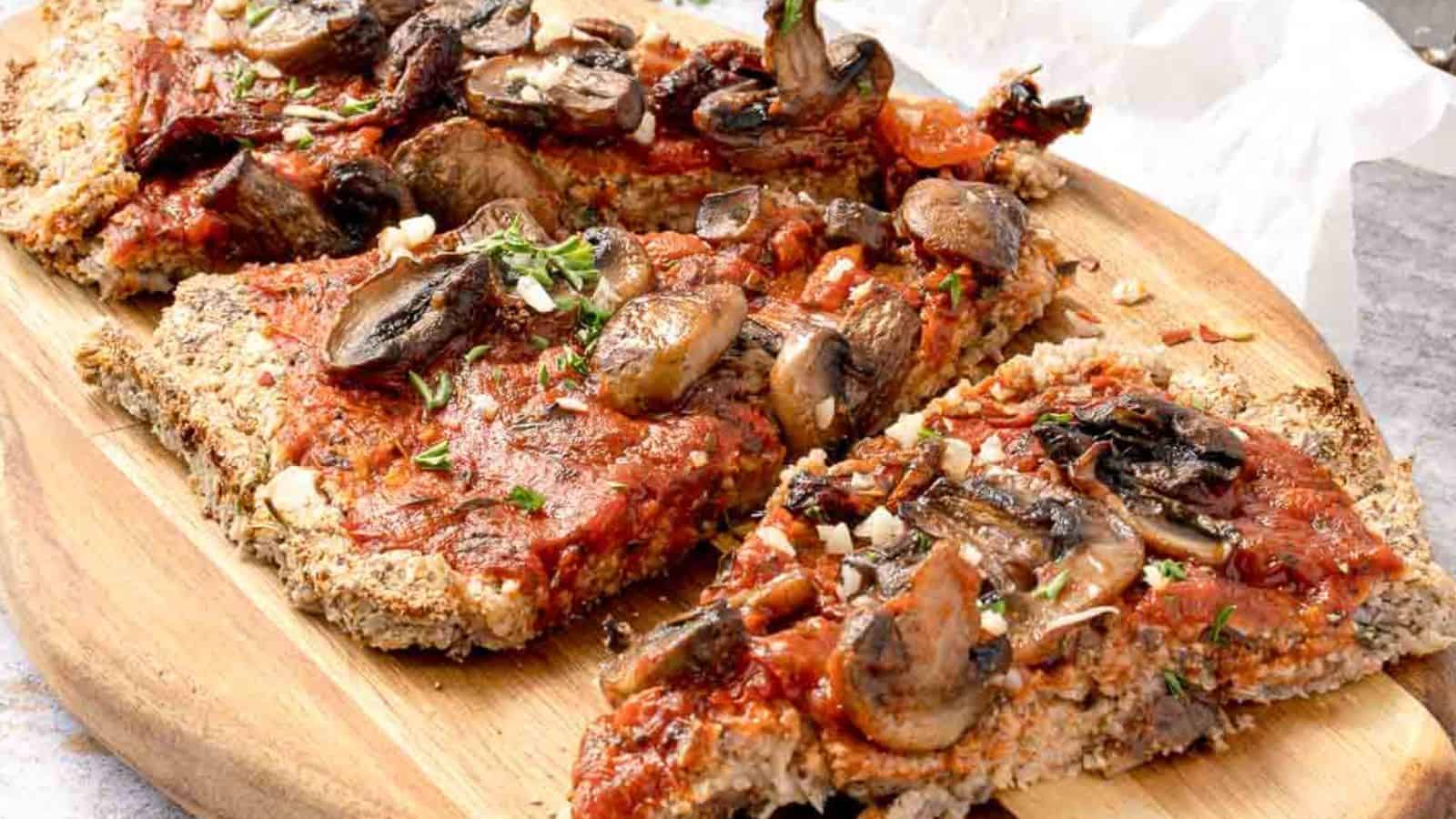 Close-up of vegan cauliflower pizza crust with garlicky mushroom & tomato topping in a wooden board.