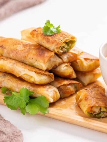 An image of vegan egg rolls arranged on a serving dish with sweet chili sauce on the side.