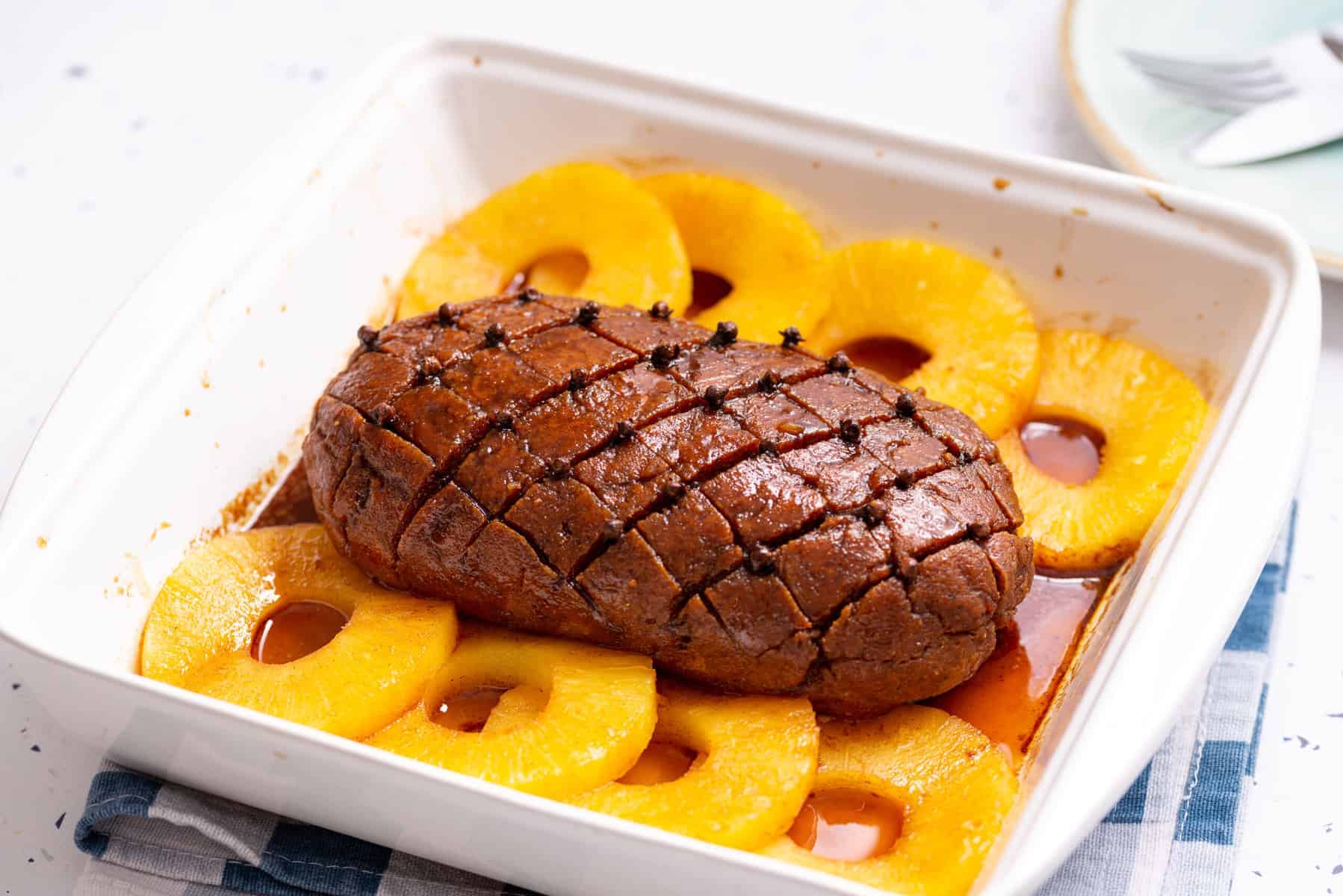 Overhead photo of vegan ham with pineapple slices placed on a white serving dish.