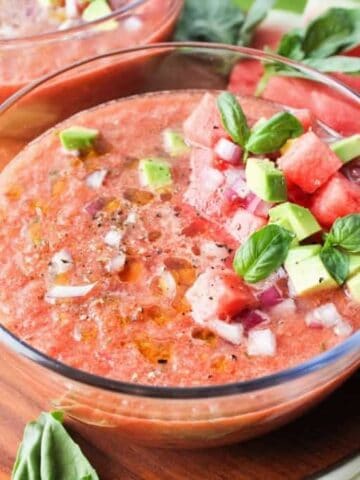 A bowl with watermelon rind gazpacho topped with red onion, fresh herbs, and diced avocado.