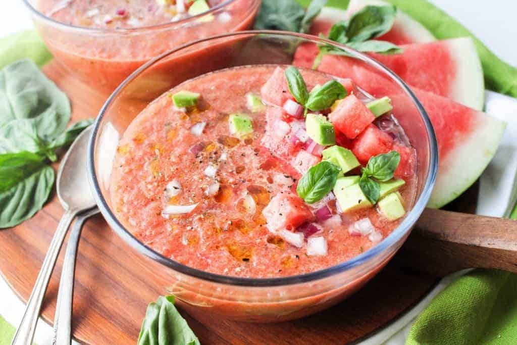 A bowl with watermelon rind gazpacho topped with red onion, fresh herbs, and diced avocado.