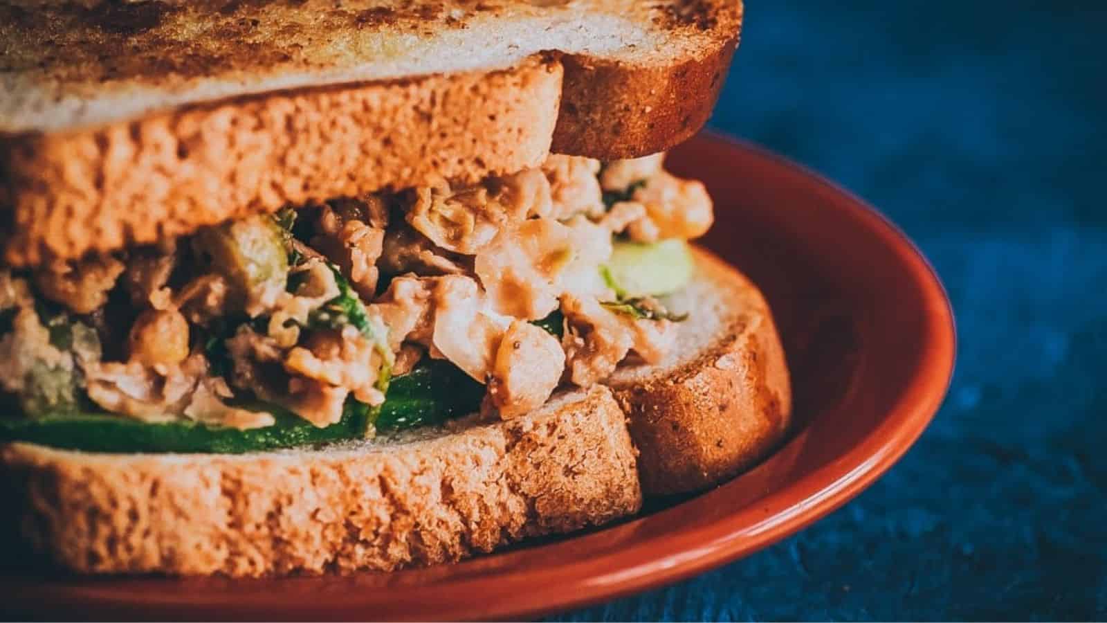 Zesty smashed chickpea salad sandwich on a red plate.