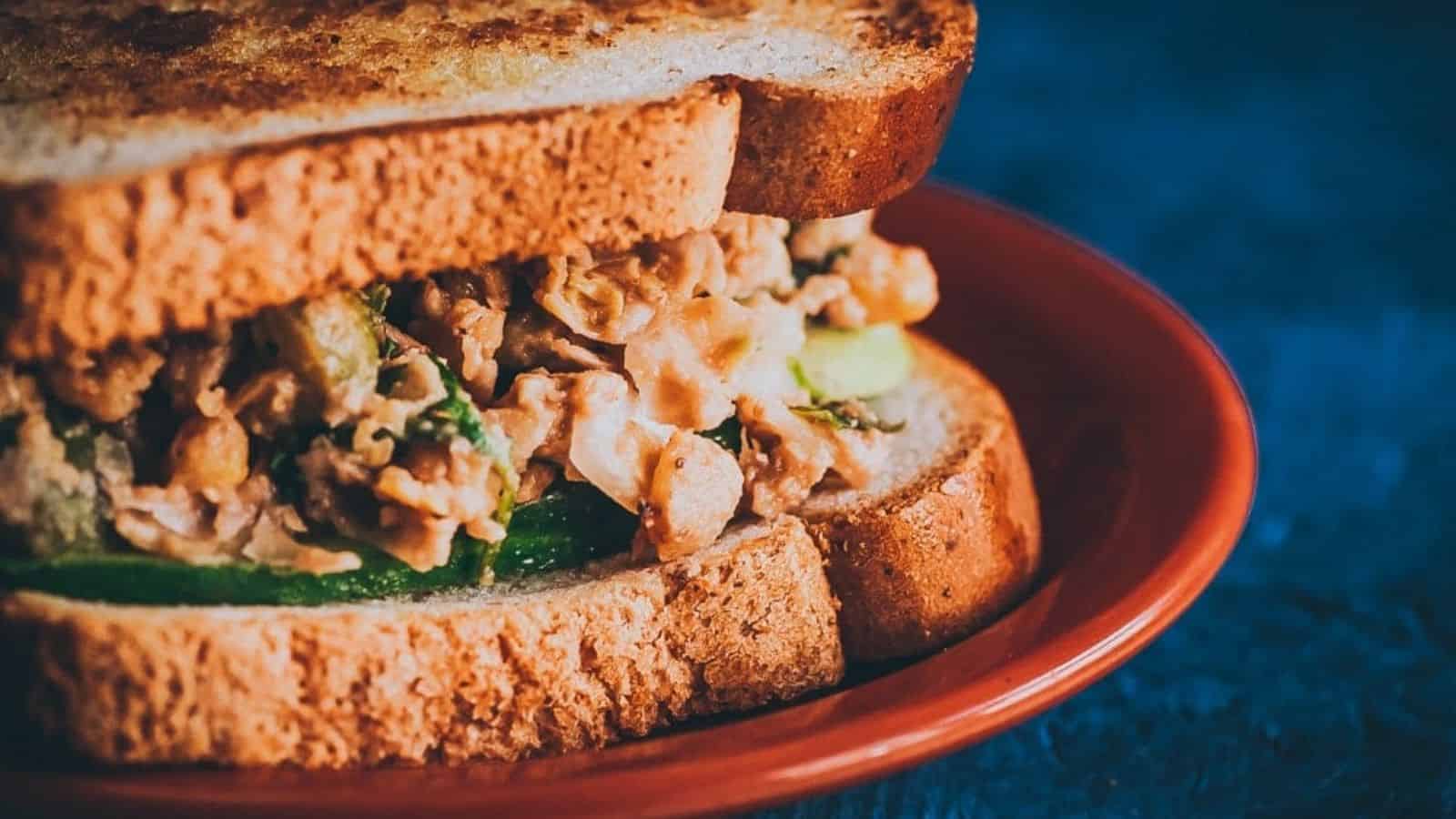 A close-up image of zesty smashed chickpea salad sandwich in a plate.