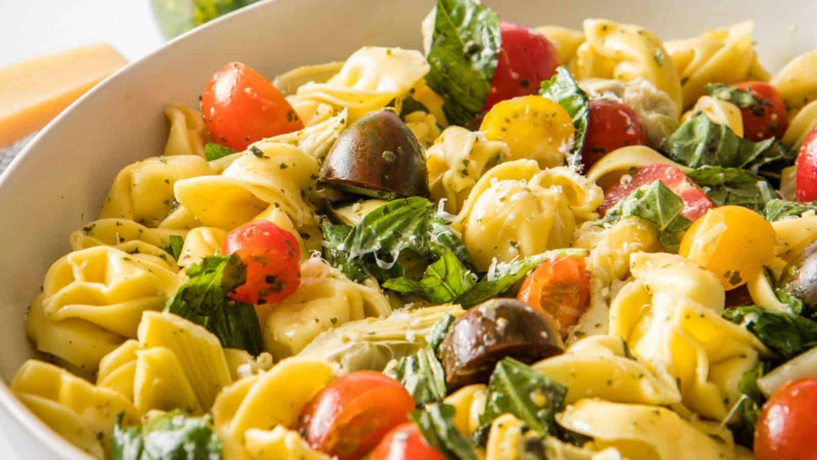 A close up view of cooked tortellini pasta salad in a white bowl.