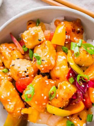 Sweet and sour tofu in a bowl with rice and chopsticks on the side.