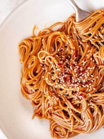 Gochujang noodles on a white plate with a fork.