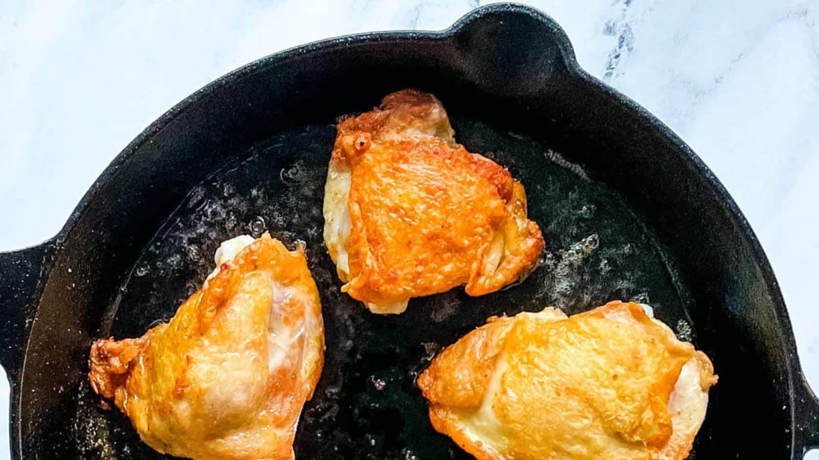 Closeup overhead shot of 3 crispy chicken thighs in a black cast iron skillet.