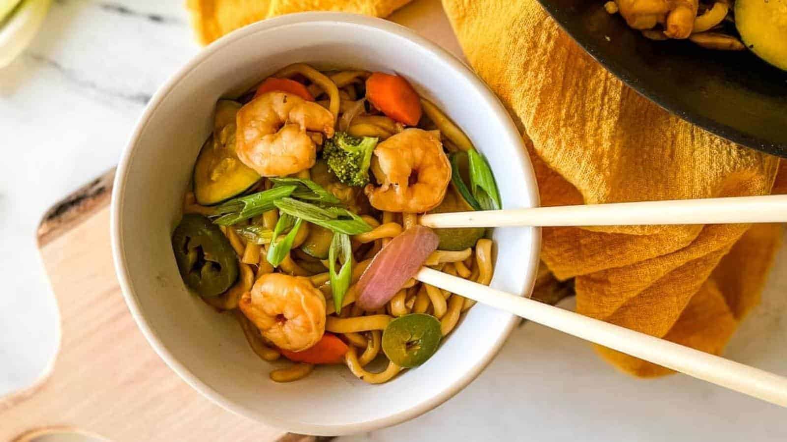 A white bowl of shrimp yaki udon with wooden chopsticks.