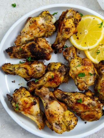 Delicious Air Fryer Lemon Pepper Chicken Wings on a white plate with lemon and parsley.