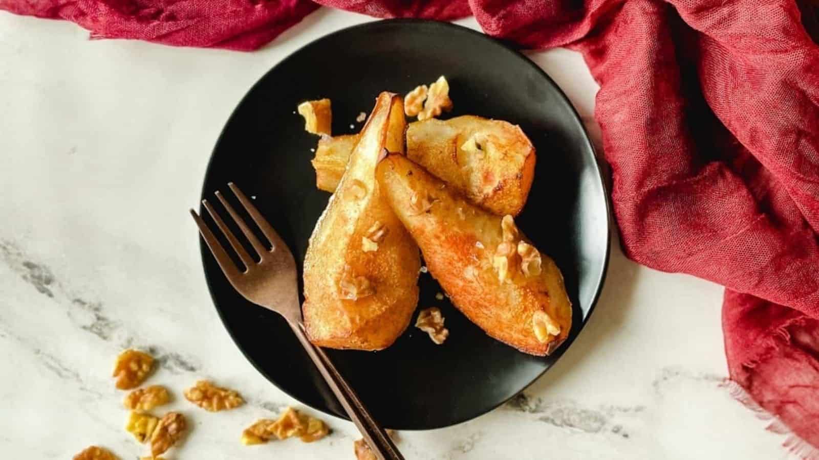 Air fryer pears sit on a black plate topped with walnuts.