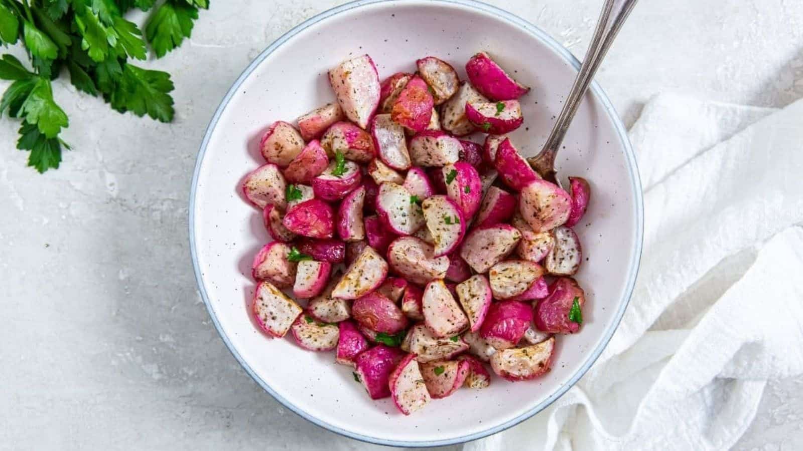 Air Fryer Radishes with parsley, salt, and pepper in a white bowl with a spoon.