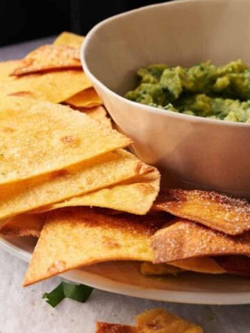 Air fried tortilla chips stacked on a plate around a bowl of dipping sauce.