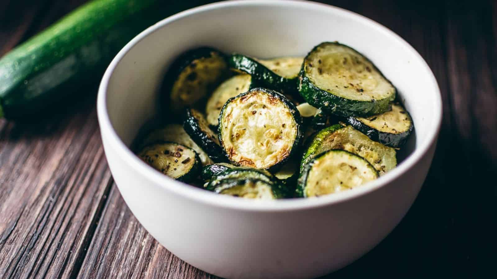 A bowl of air fryer zucchini with a whole zucchini in the background.