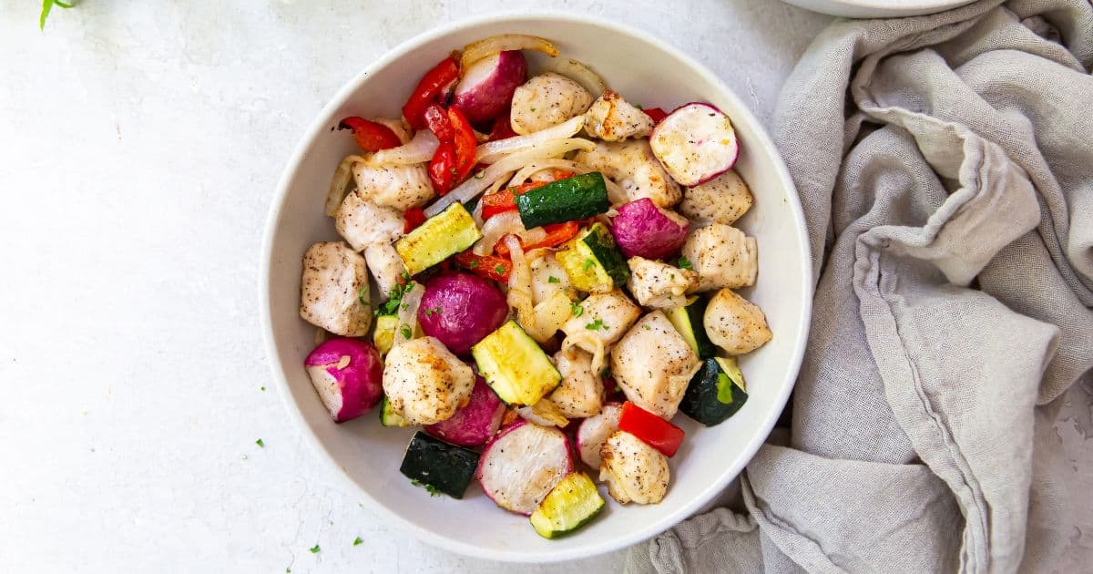 Air Fryer Chicken and Veggies in a white bowl with a fork and parsley.