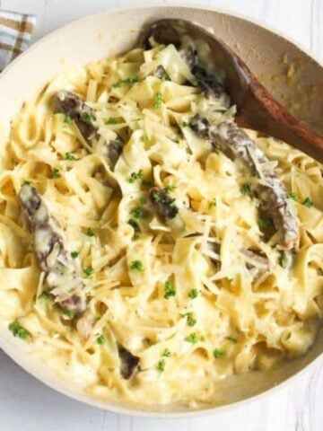 Alfredo steak pasta in skillet with wooden spoon.