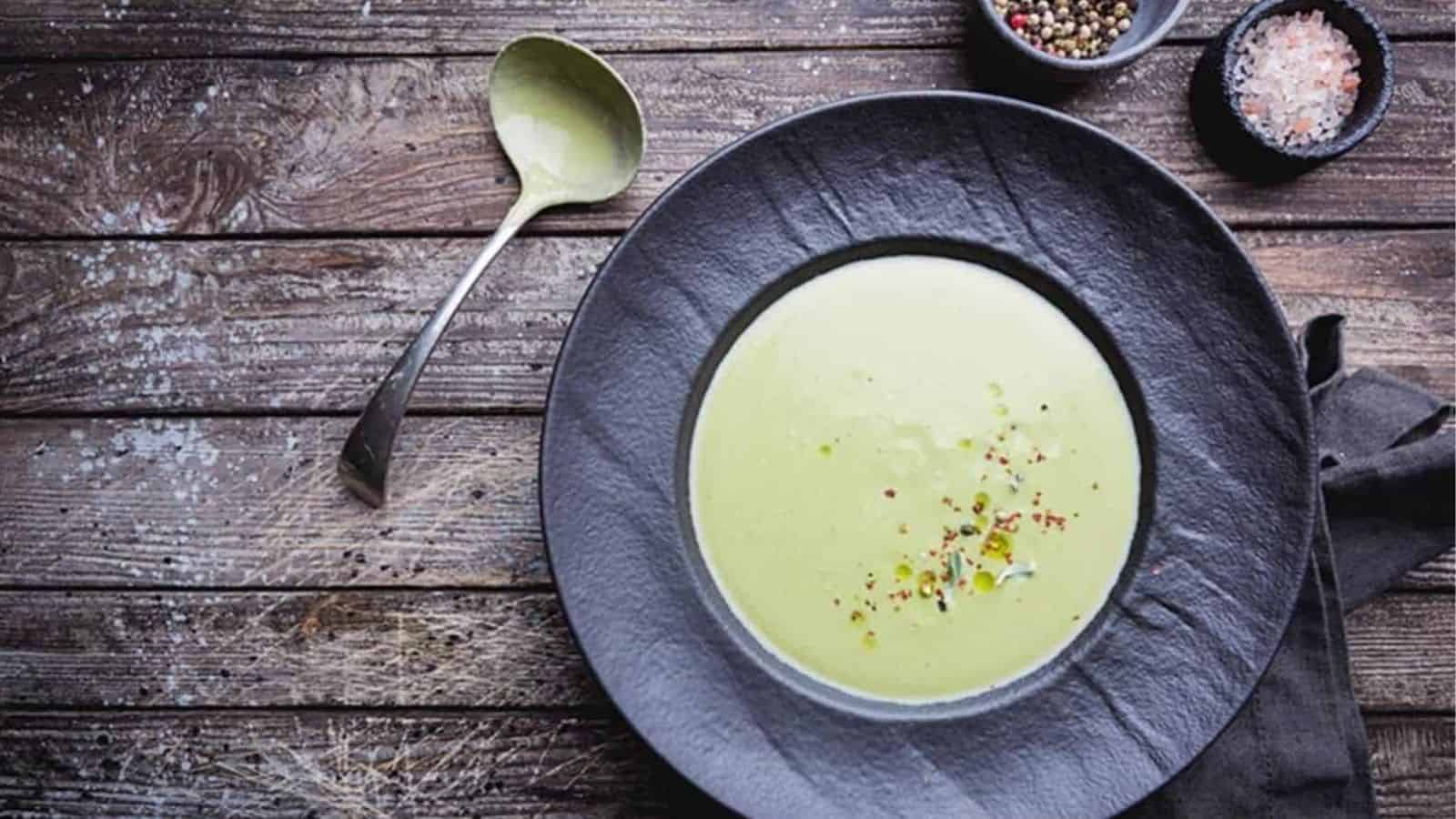 Avocado Bone Broth in black bowl with ladle on wooden background.