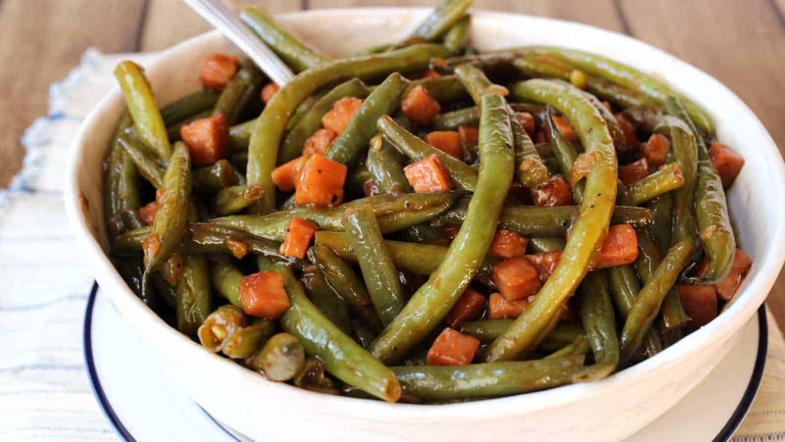 A white bowl with barbecued green beans and chuncks of ham.