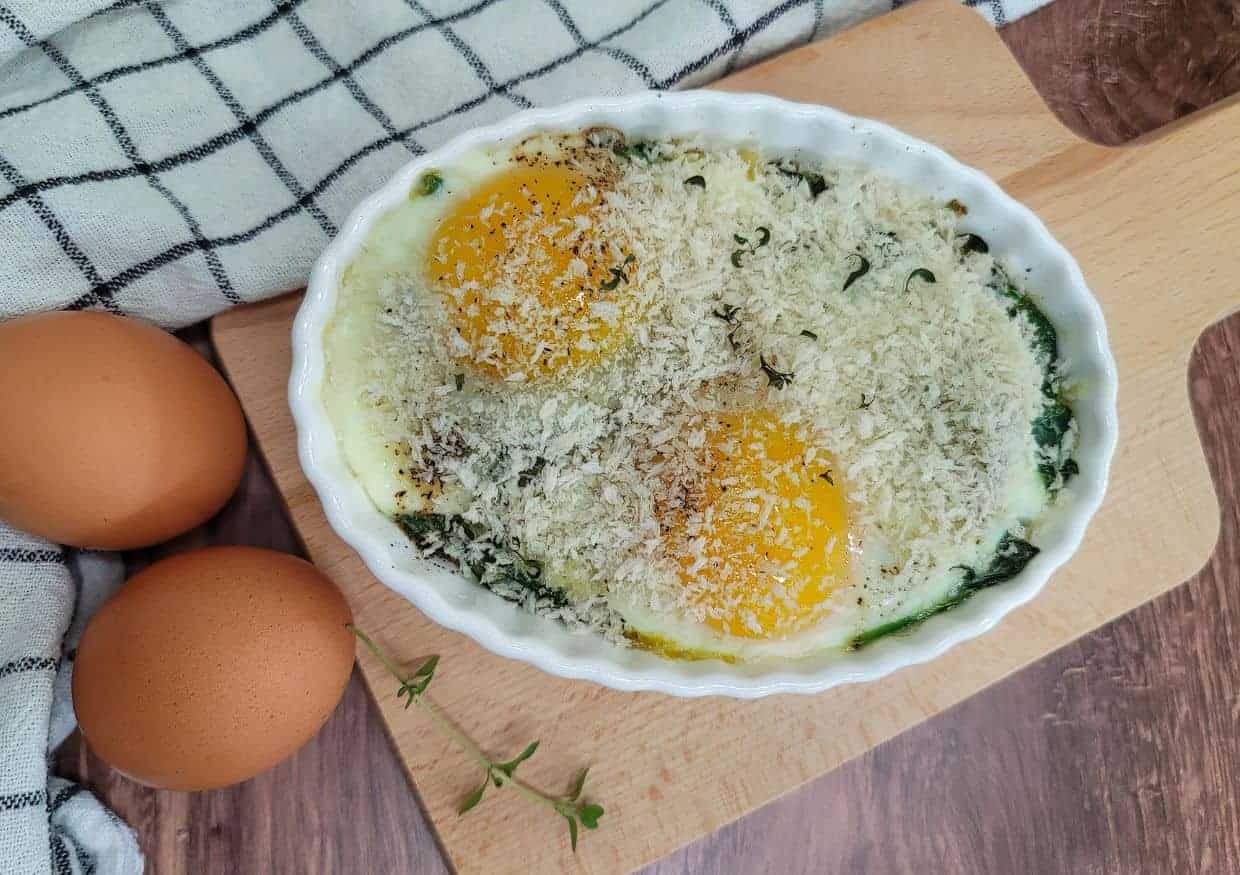 A gratin dish of baked eggs on a bed of sauteed spinach.