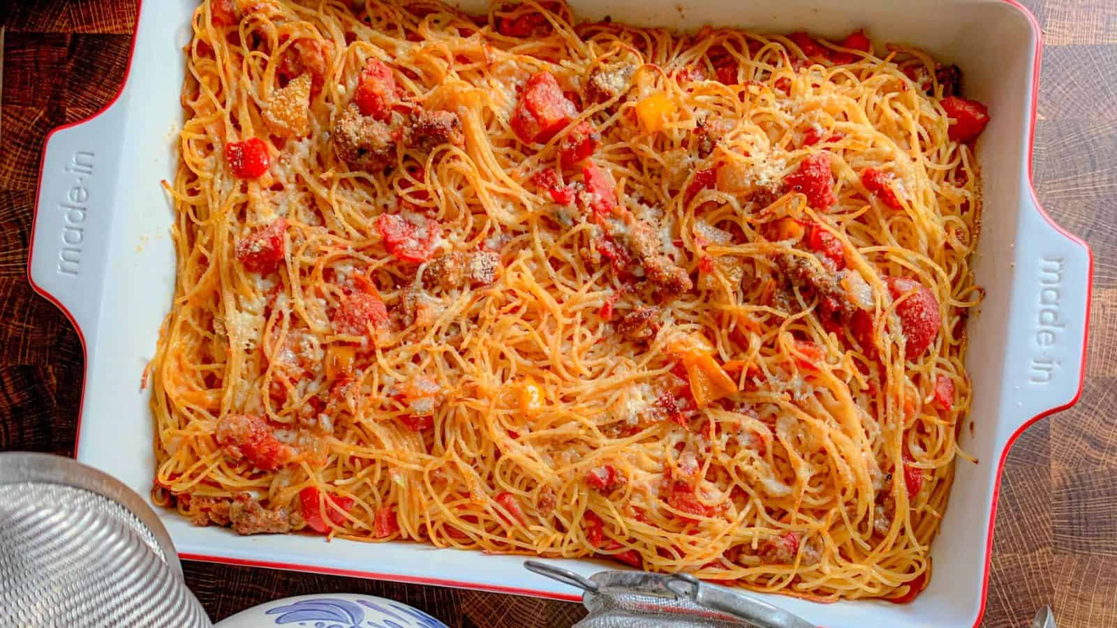 A spaghetti noodles casserole in a baking dish with peppers, tomatoes, and cheese.