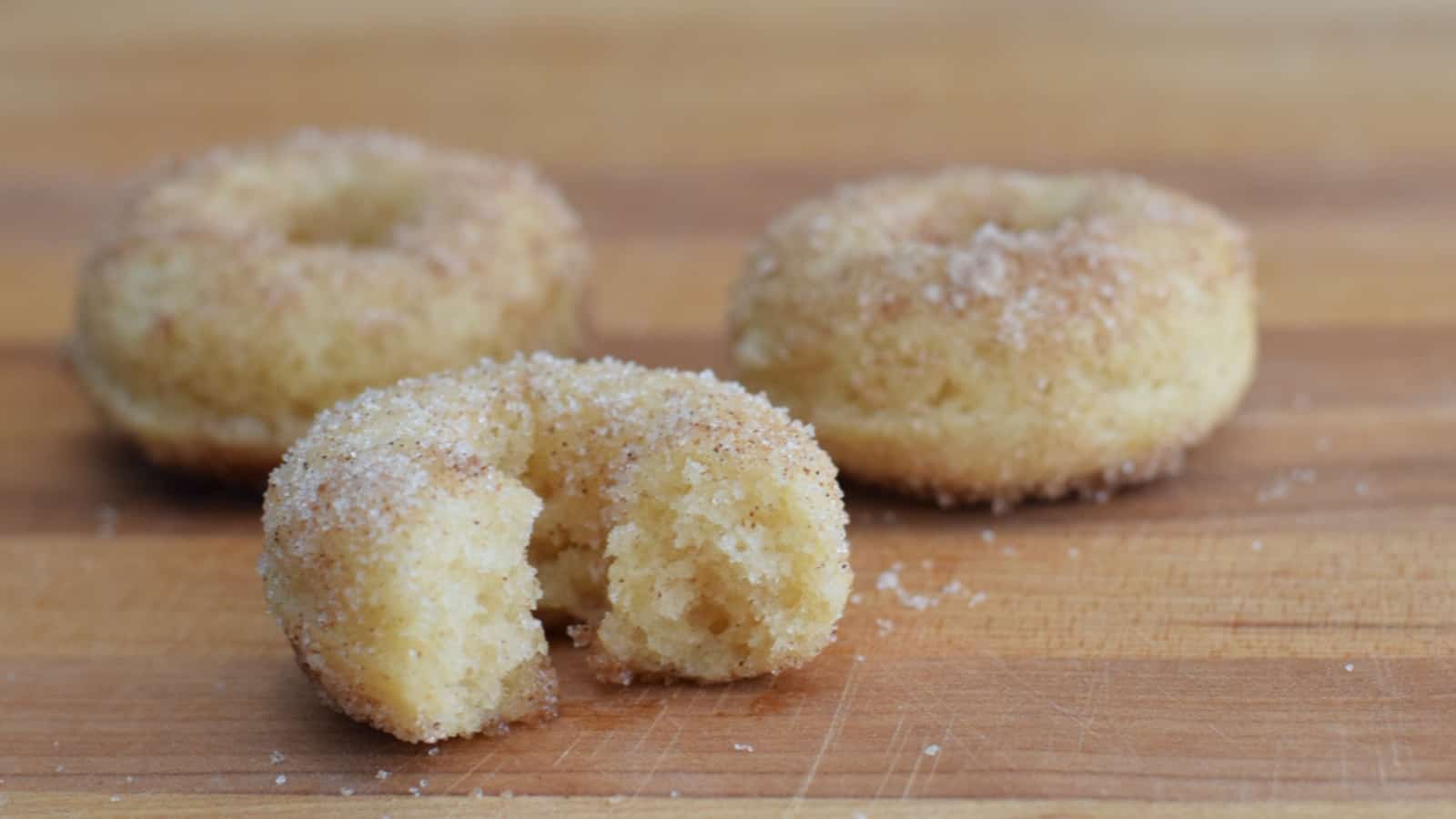 Image shows baked cinnamon sugar donuts on a wooden table.